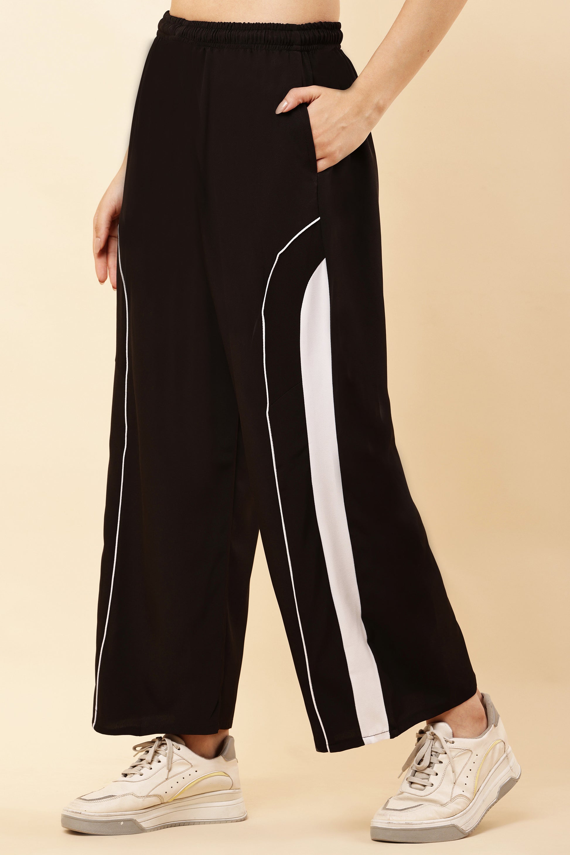 Black pants with white stripes worn by a person on a beige background